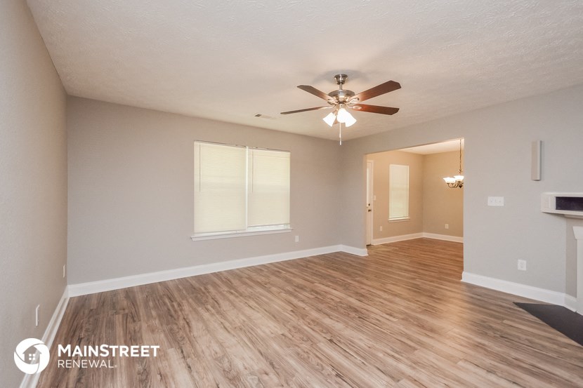 the spacious living room with hardwood flooring and a ceiling fan