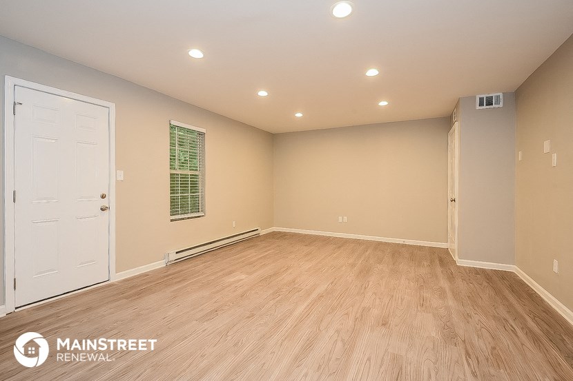 the spacious living room with wood flooring and a white door