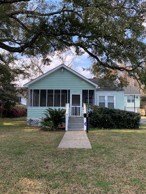 A green house with a porch and a tree in front.