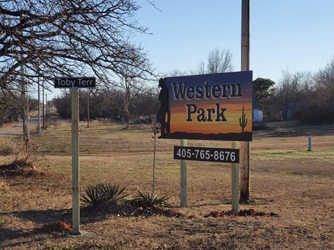A sign for Western Park stands in a field with a tree and a smaller sign reading Toby Terra.