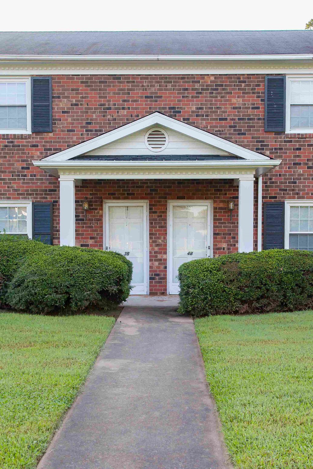 the front of a brick house with two doors and a sidewalk
