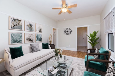 A living room with a white couch, a glass coffee table, and a ceiling fan.