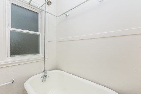A white bathtub with a shower head and a window.