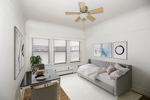 A modern bedroom with a bed, a dining table, and a ceiling fan.