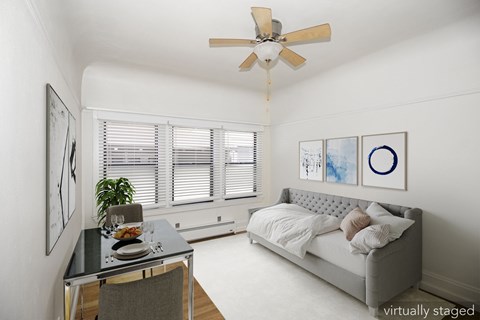 A modern bedroom with a bed, a table, a ceiling fan, and artwork on the wall.