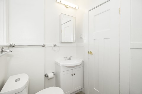 A white bathroom with a toilet, sink, and mirror.