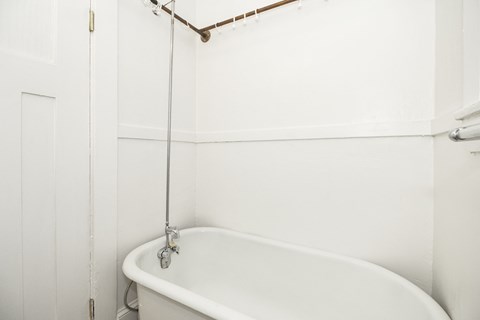 A white bathtub with a shower head attached to the wall.