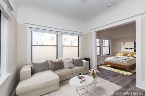 A living room with a couch, a coffee table, and a bed in the background.