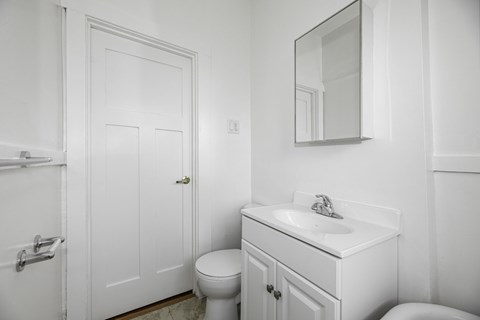 A white bathroom with a toilet, sink, and mirror.