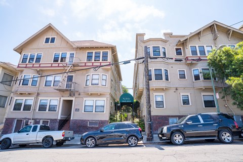A row of apartment buildings with cars parked in front.