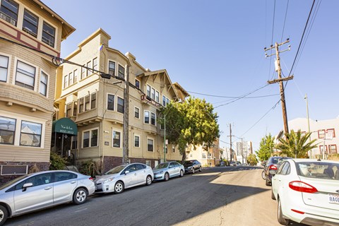Cars parked on a street in front of apartment buildings.