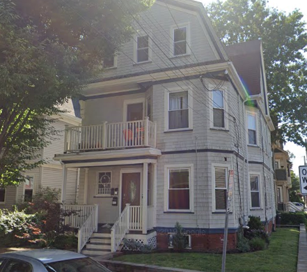 a white house with a porch on the corner of a street