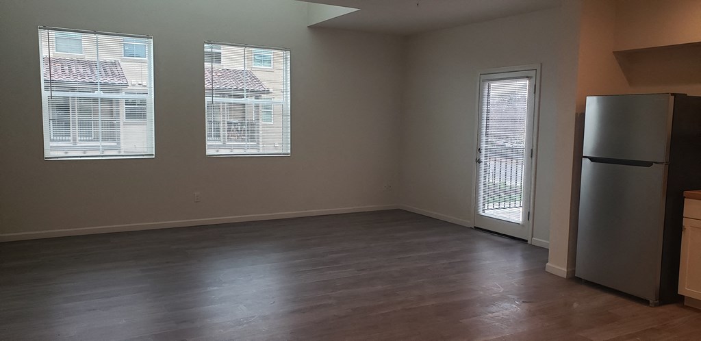 an empty living room with a refrigerator and three windows