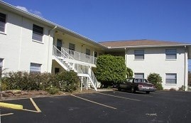 A car is parked in a parking lot in front of a white building.