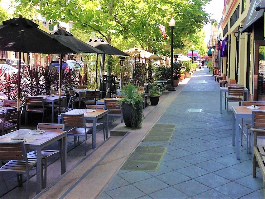a sidewalk filled with tables and chairs and umbrellas