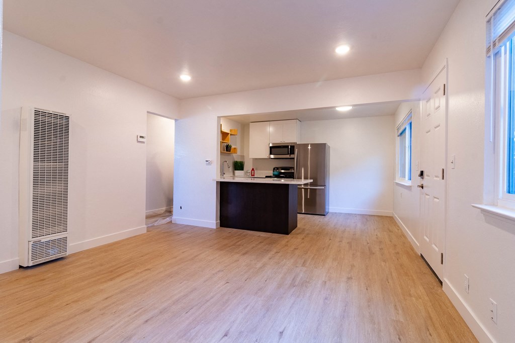 an empty living room and kitchen with wood floors and a refrigerator