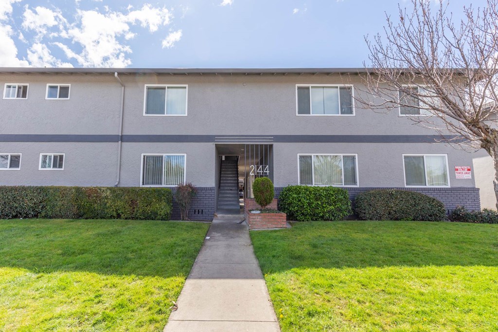 the front of an apartment building with a sidewalk and grass