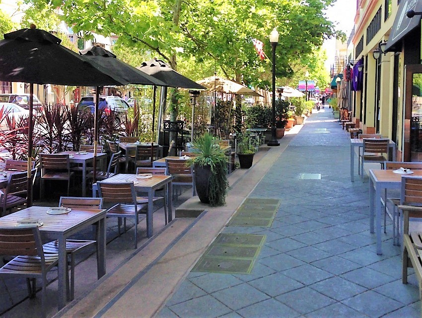 a sidewalk filled with tables and chairs and umbrellas