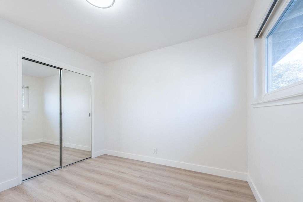 an empty bedroom with a mirrored closet door and a window