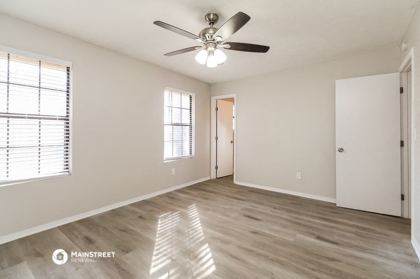 the spacious living room with a ceiling fan and white walls