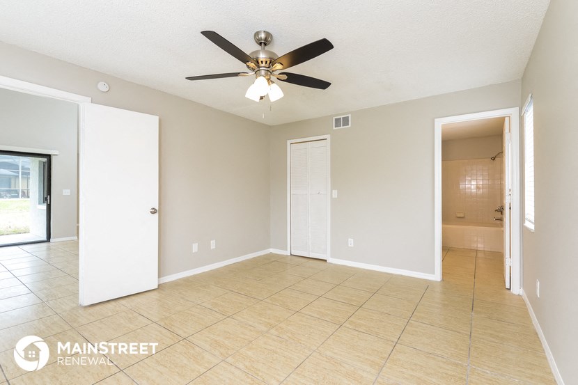 an empty living room with a ceiling fan and a door to a bathroom