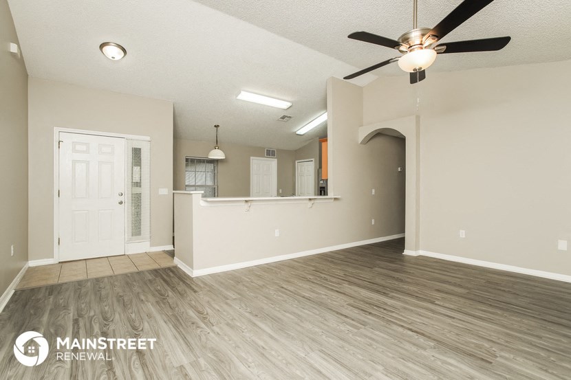 the living room and kitchen of an empty house with a ceiling fan