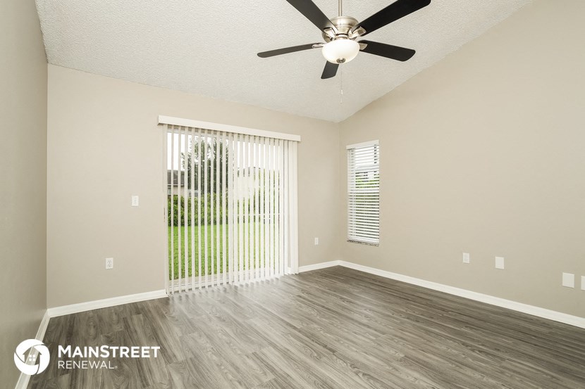the spacious living room with wood flooring and a ceiling fan