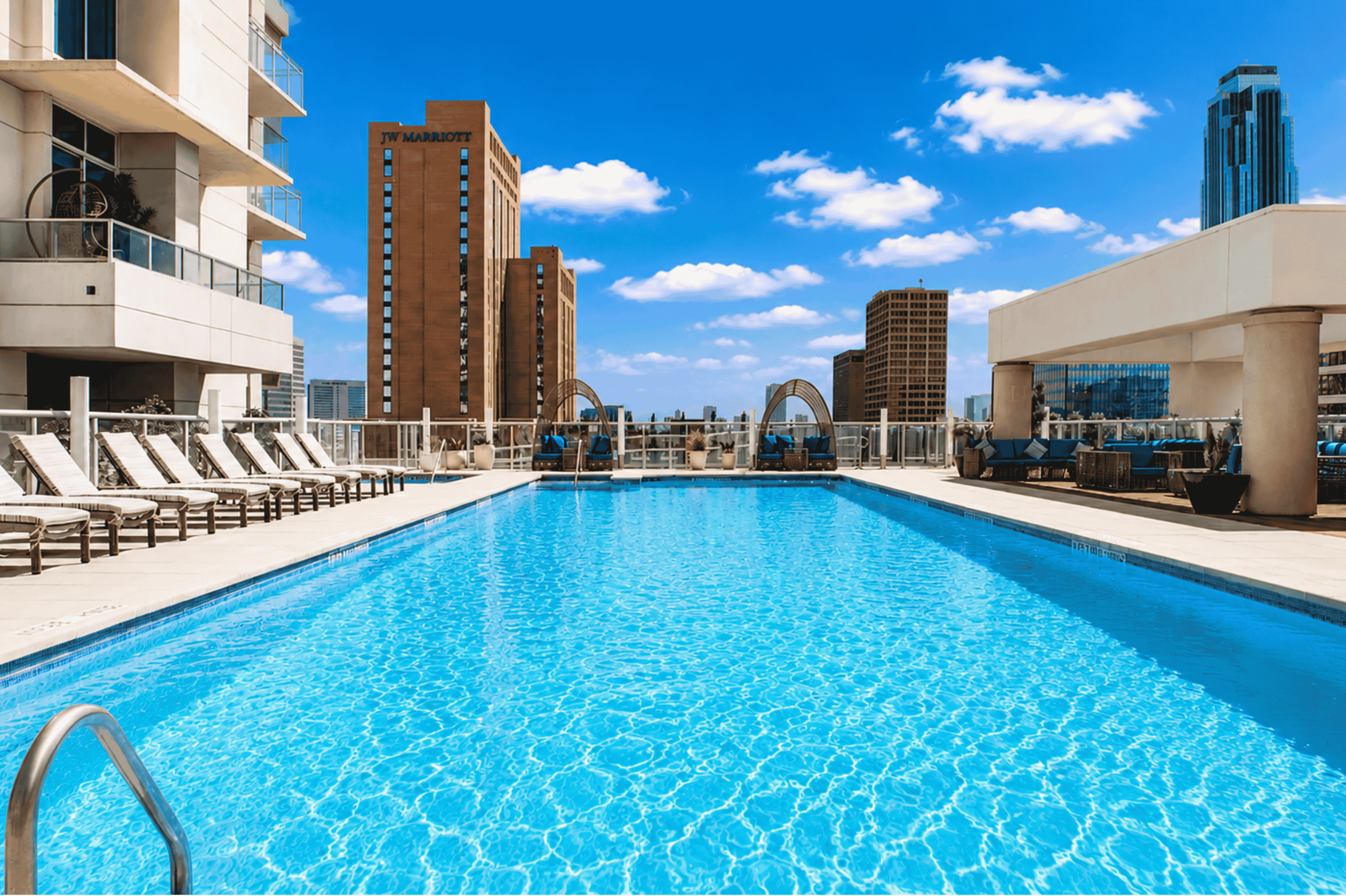 A large swimming pool in a hotel with lounge chairs and buildings in the background.