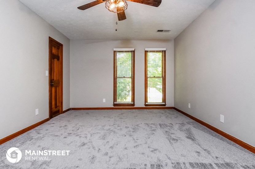 an empty living room with a ceiling fan and two windows