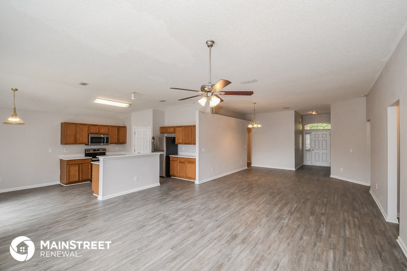 the living room and kitchen of an apartment with wood flooring and a ceiling fan