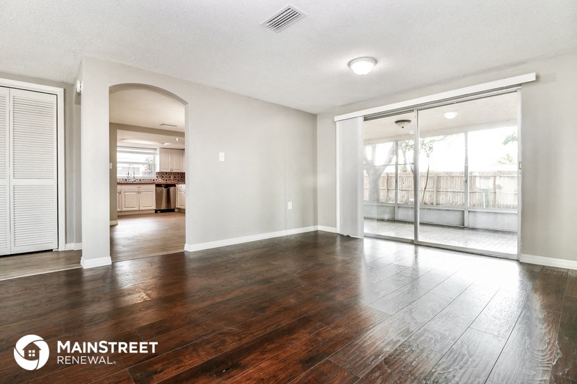 an empty living room with wood flooring and sliding glass doors to a kitchen