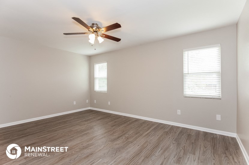 the spacious living room with wood flooring and a ceiling fan