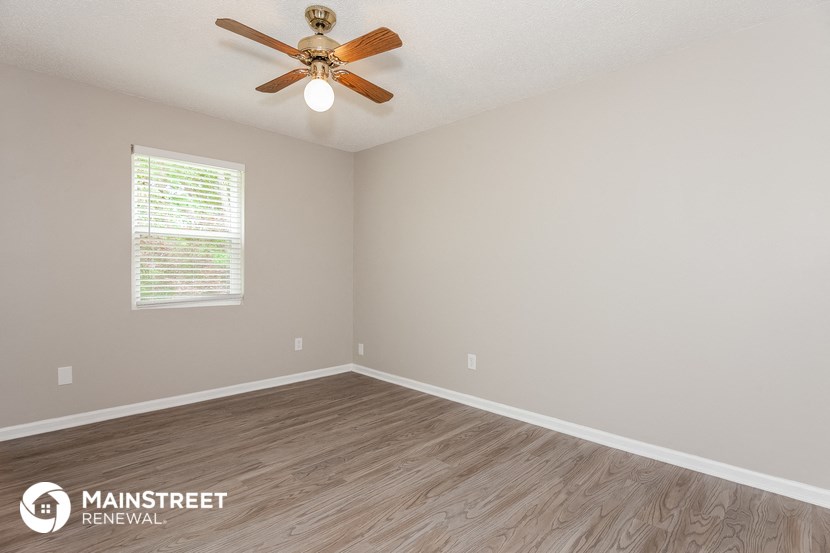 the spacious living room with wood flooring and a ceiling fan