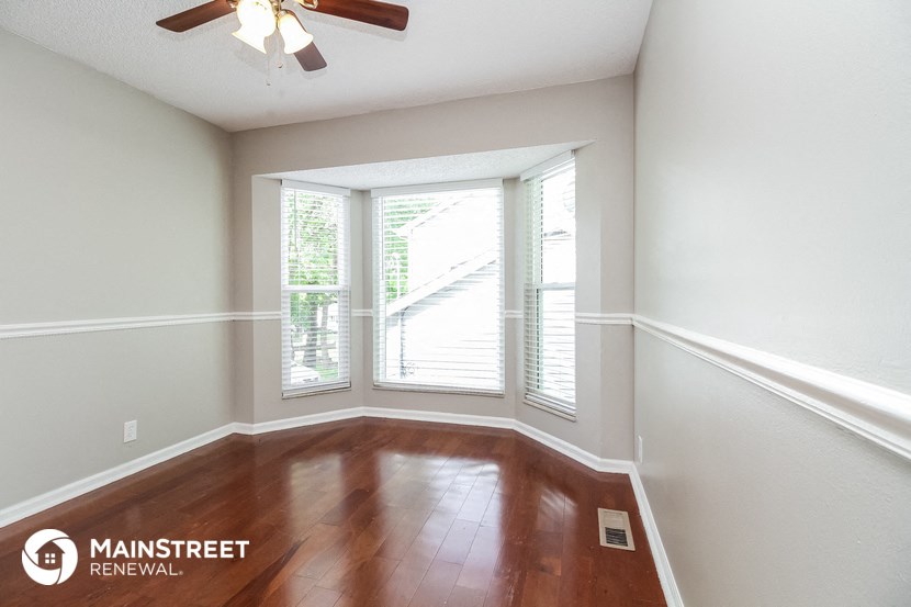 a living room with a large window and wooden floors and a ceiling fan