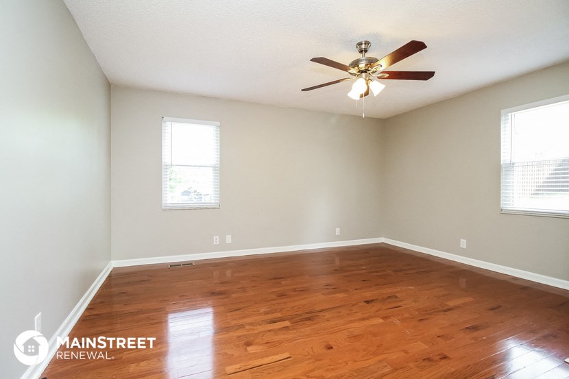 the spacious living room with hardwood flooring and a ceiling fan