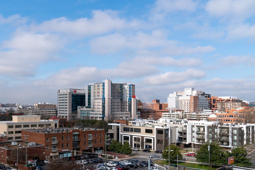 A cityscape with buildings of various heights and a parking lot in the foreground.