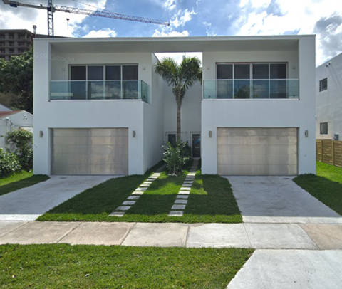 a white house with two garage doors and a palm tree