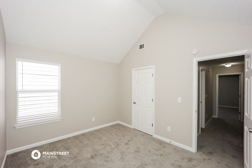 the spacious bedroom with a door to the hallway and carpeted flooring