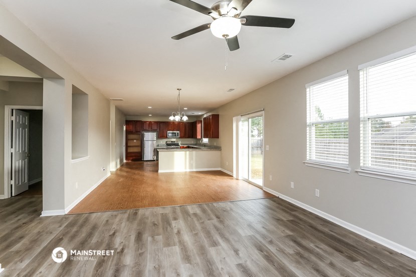 an empty living room and kitchen with wood flooring and a ceiling fan