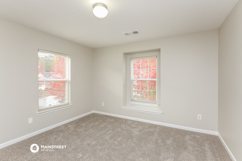 an empty room with two windows and carpeting