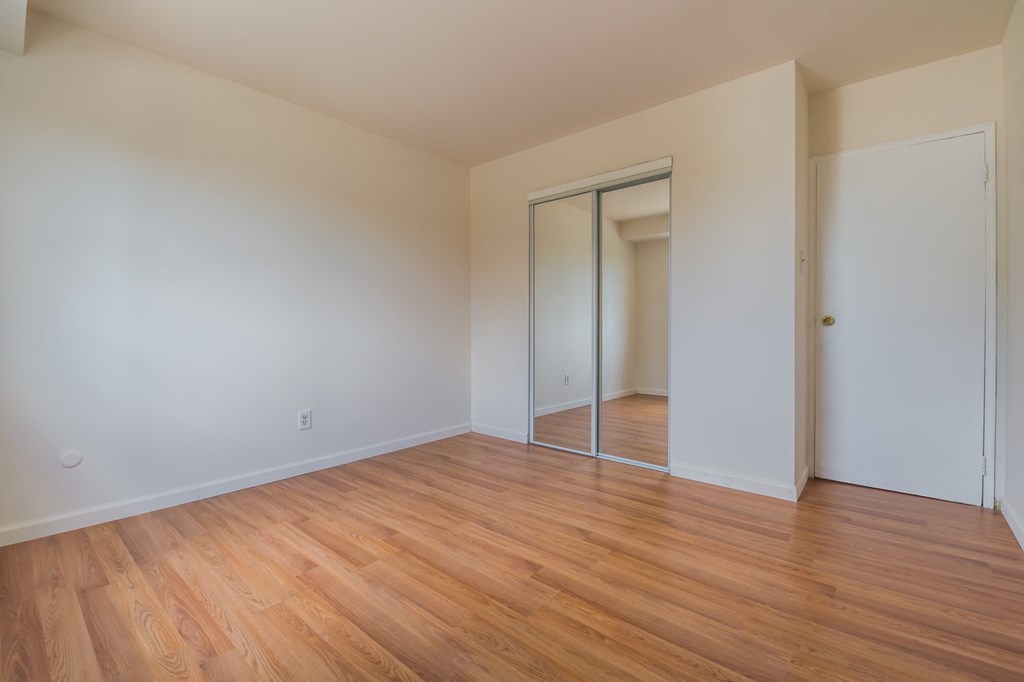 an empty living room with wood flooring and a mirrored closet