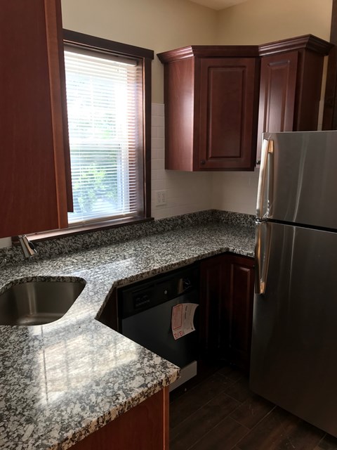 A kitchen with a granite counter top and a stainless steel refrigerator.