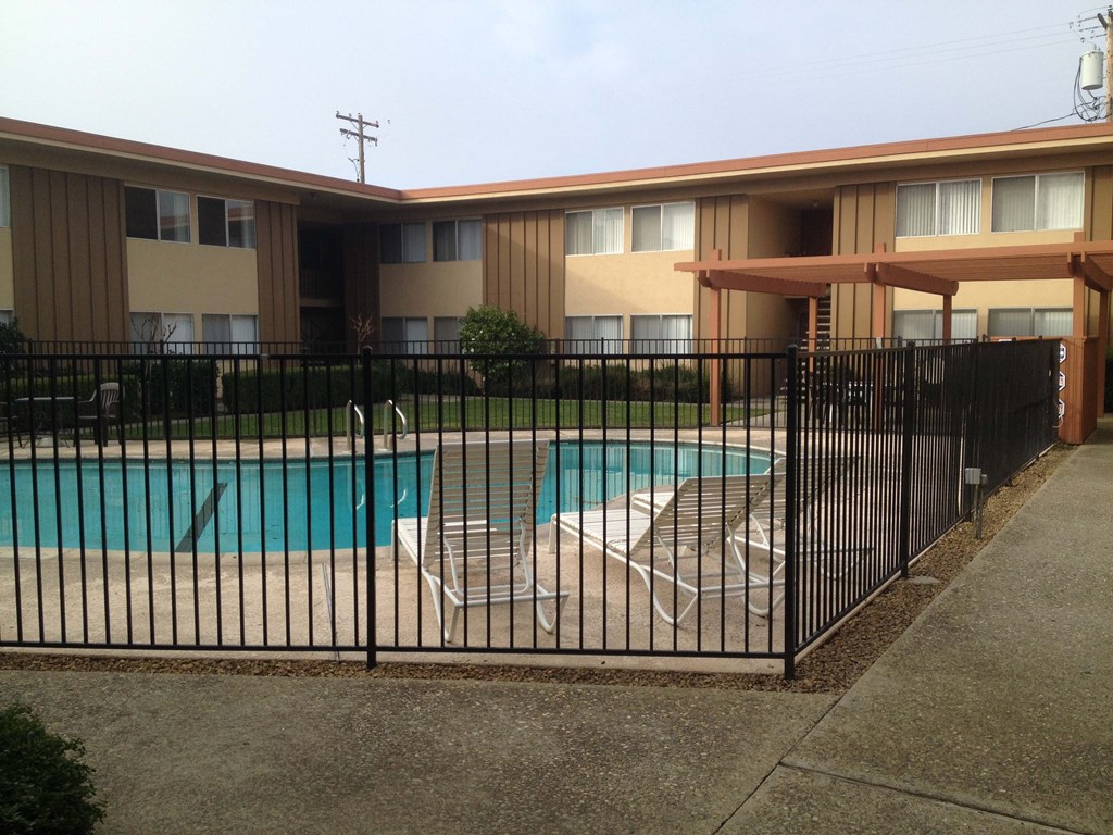 a pool with two lounge chairs behind a wrought iron fence