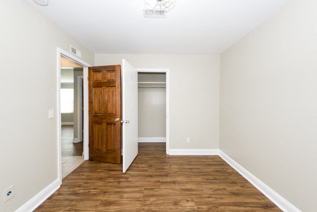 an empty room with a wooden door and a hallway to a closet