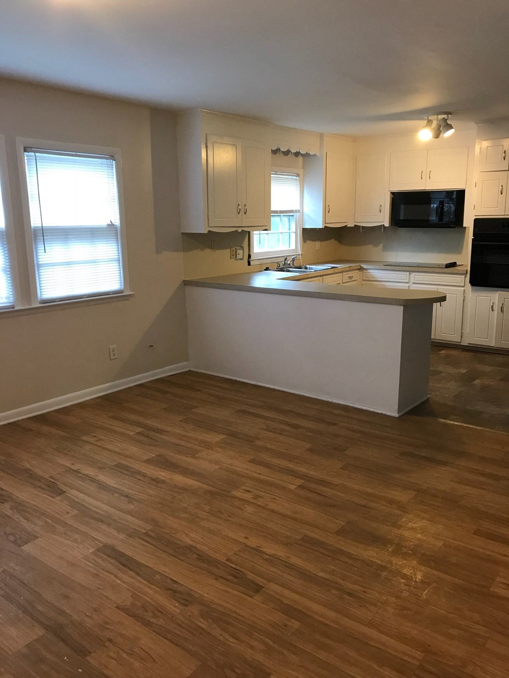 an empty kitchen with white cabinets and a wooden floor