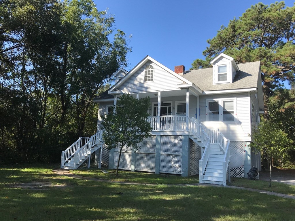 A white house with a porch and a staircase leading to the second floor.