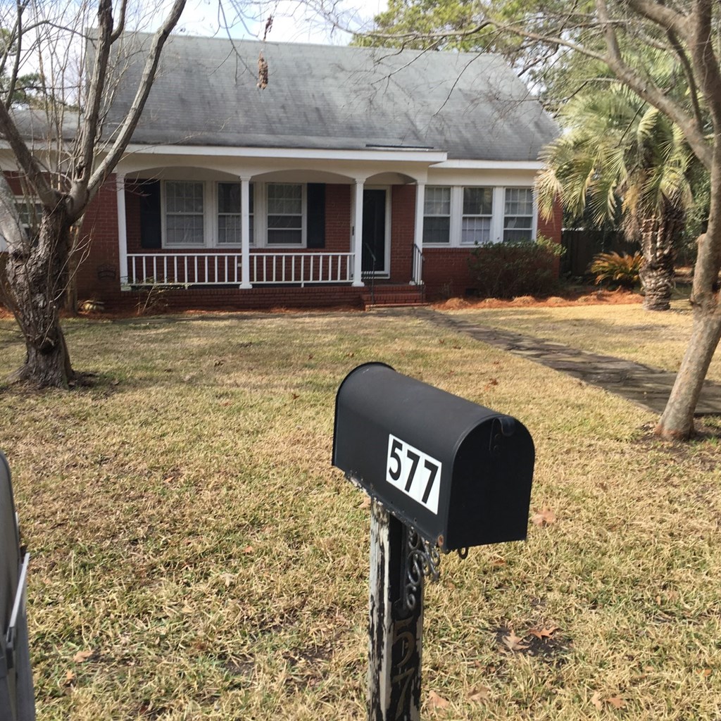 A black mailbox with the number 577 on it in front of a house.