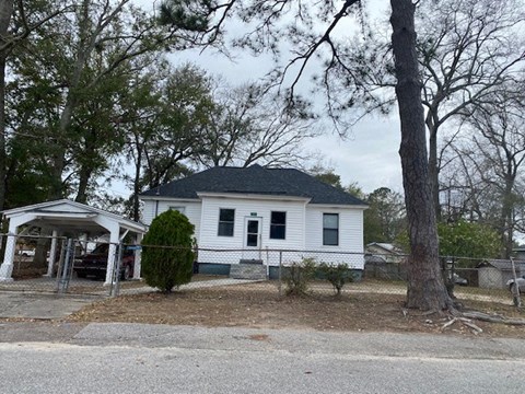 A white house with a black roof is surrounded by trees and a fence.