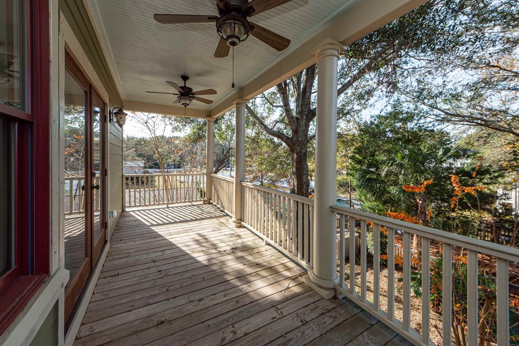 A porch with a ceiling fan and a view of trees.