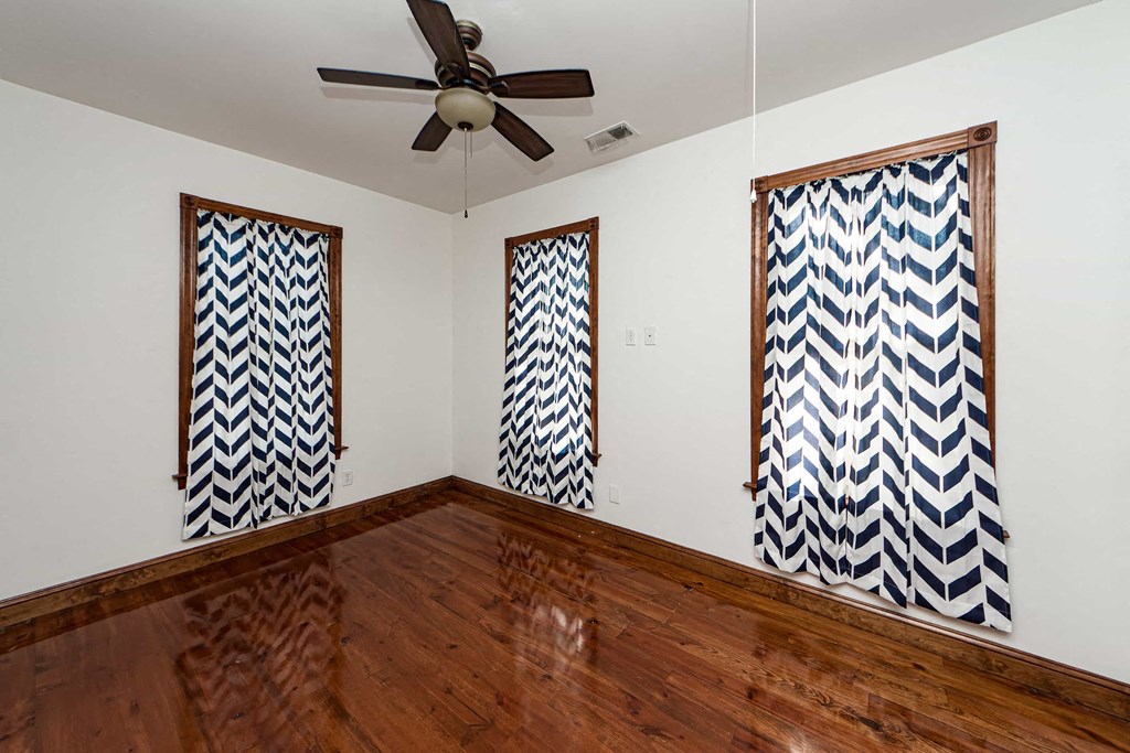 A room with a wooden floor and three patterned windows.